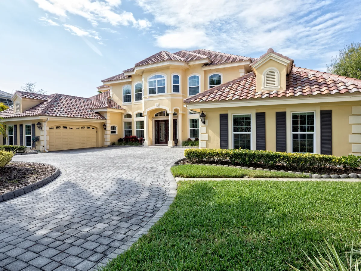 Gray paver driveway with a darker edge course sweeping up to a tile roofed home