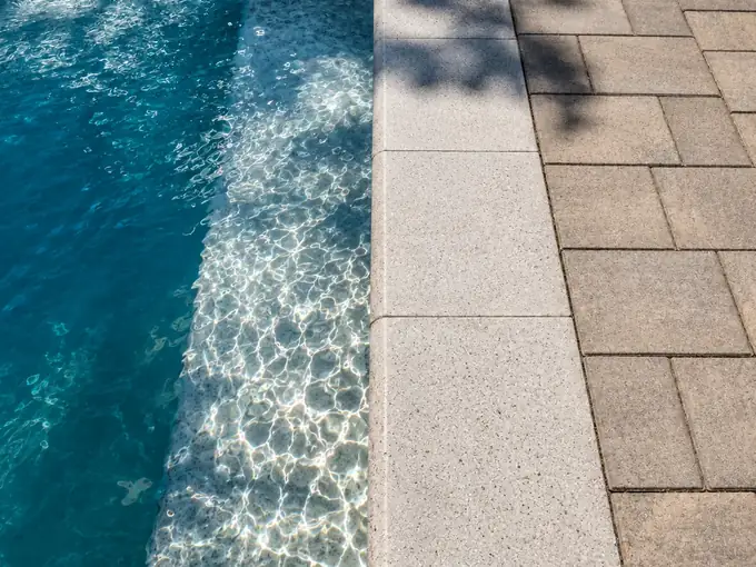 Pool edge with light bullnose coping beside a tan paver deck laid in running bond