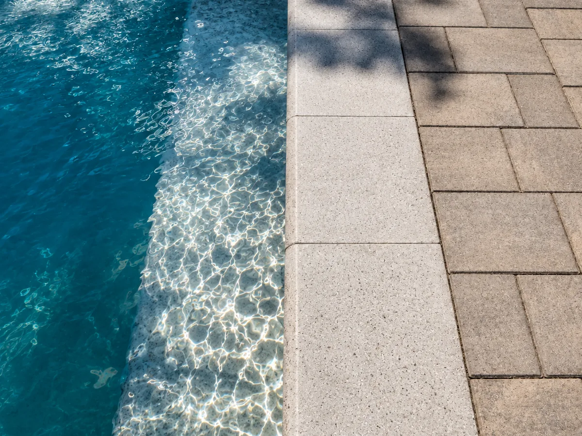Pool edge with light bullnose coping beside a tan paver deck laid in running bond